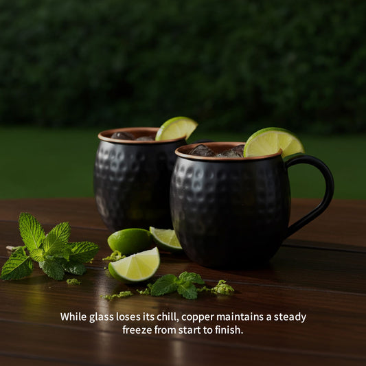 Two copper mugs with drinks and lime wedges on a wooden surface with a green blurred background.