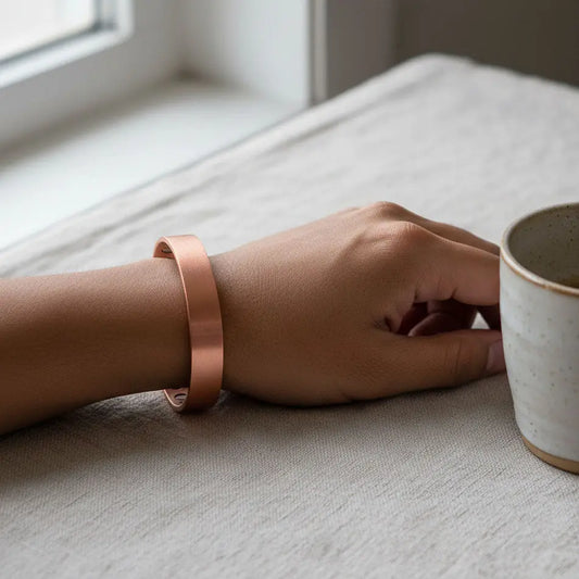 Hand wearing a copper bracelet on a light surface with a cup nearby