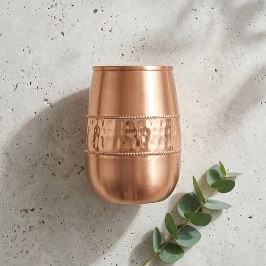 Copper cup with textured design on a light gray surface with eucalyptus leaves.