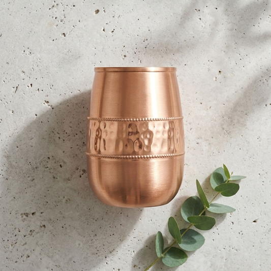 Copper cup with textured design on a light gray surface with eucalyptus leaves.