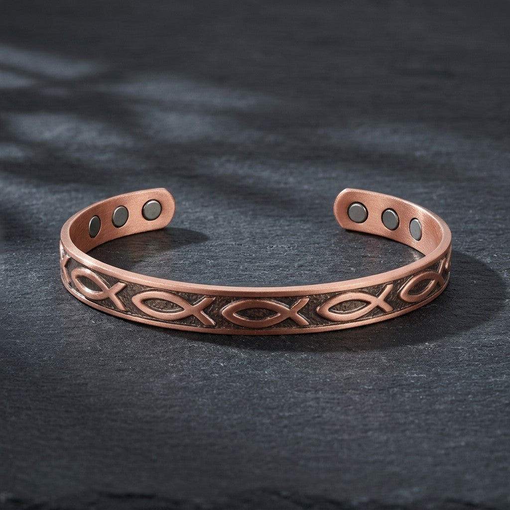 A copper magnetic cuff bracelet with a fish motif, displayed on a dark slate surface.