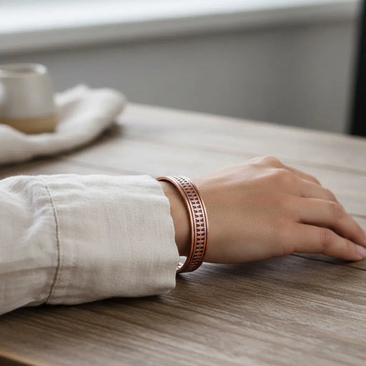 Person wearing a arrow copper bracelet on a wooden table with a blurred background