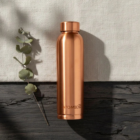 Copper water bottle with 'Atomic29' branding on a textured surface with a plant.