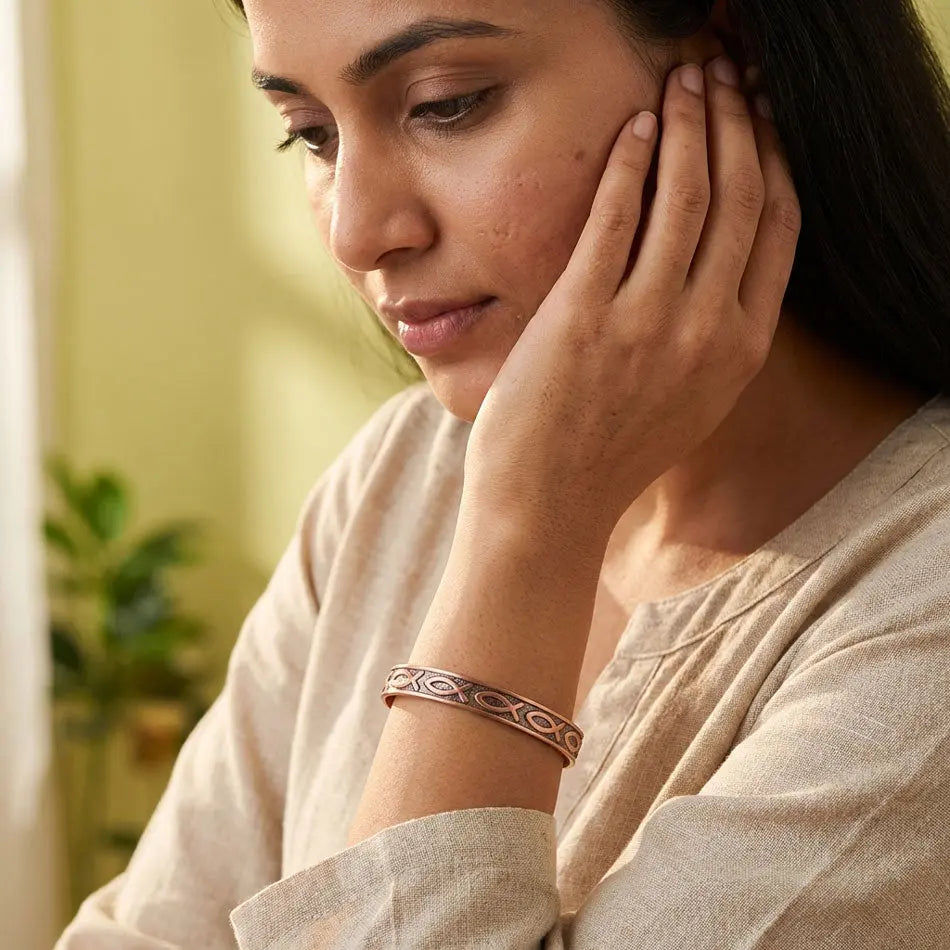 Woman wearing a copper bracelet, looking thoughtful with a blurred indoor background