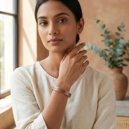 Woman wearing a copper bracelet in a warm-toned room with a plant