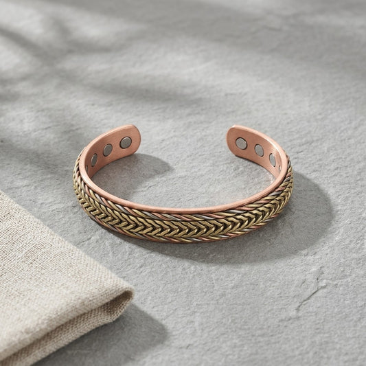 Braided copper magnetic cuff bracelet with a braided bronze and copper, displayed on a grey textured surface next to a folded beige fabric.