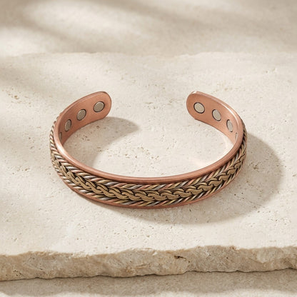 Braided copper cuff bracelet with a interlock patterned of brass, copper and cupronickel, displayed on a textured beige stone.