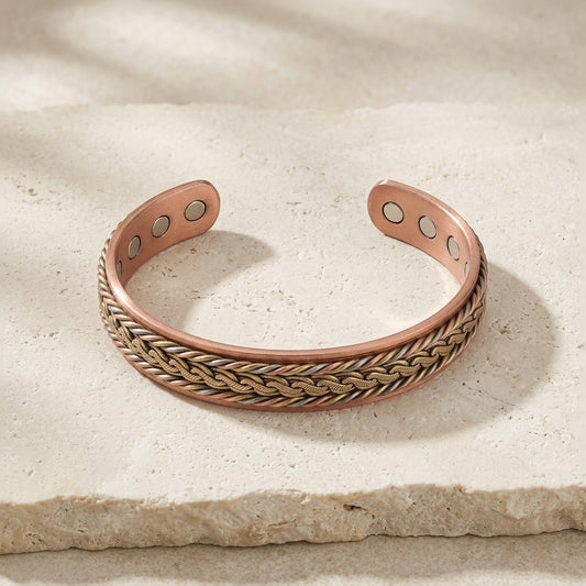 Braided copper cuff bracelet with a interlock patterned of brass, copper and cupronickel, displayed on a textured beige stone.