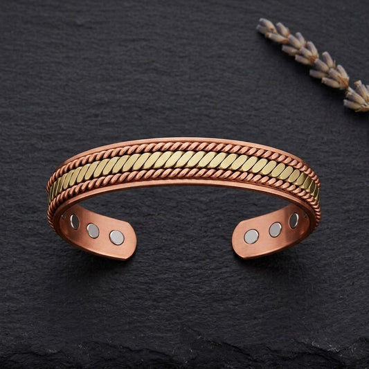 A braided copper cuff bracelet with a textured brass braided centre band, displayed on a dark slate surface with a dried lavender sprig in the background.