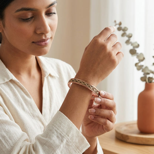A woman wearing a delicate braided copper cuff bracelet, shown in a warm, softly-lit indoor setting.