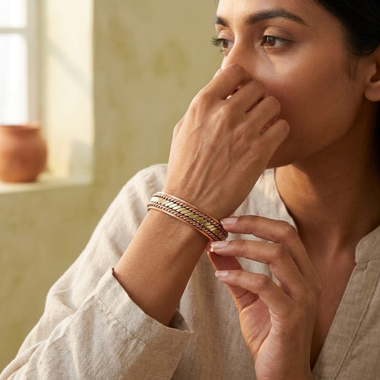 A woman wearing copper bracelet with copper and bronze braided pattern inlay, shown in a warm, softly lit indoor setting.