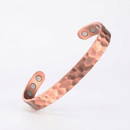 A hammered copper cuff bracelet with three circular magnetic therapy inserts on each end, displayed on a clean white background.