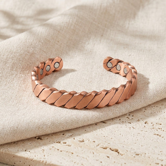 HELIX copper magnetic cuff bracelet with segmented design, displayed on a beige linen fabric surface.