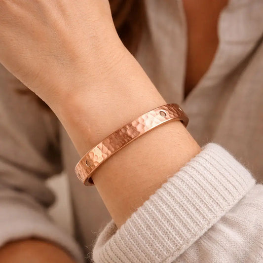 Hammered copper bracelet on a wrist with a neutral background
