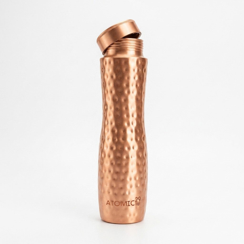 A copper water bottle with a hammered texture and a matching flip-top lid, standing upright on a white background. The brand name 'ATOMIC29' is printed near the bottom.