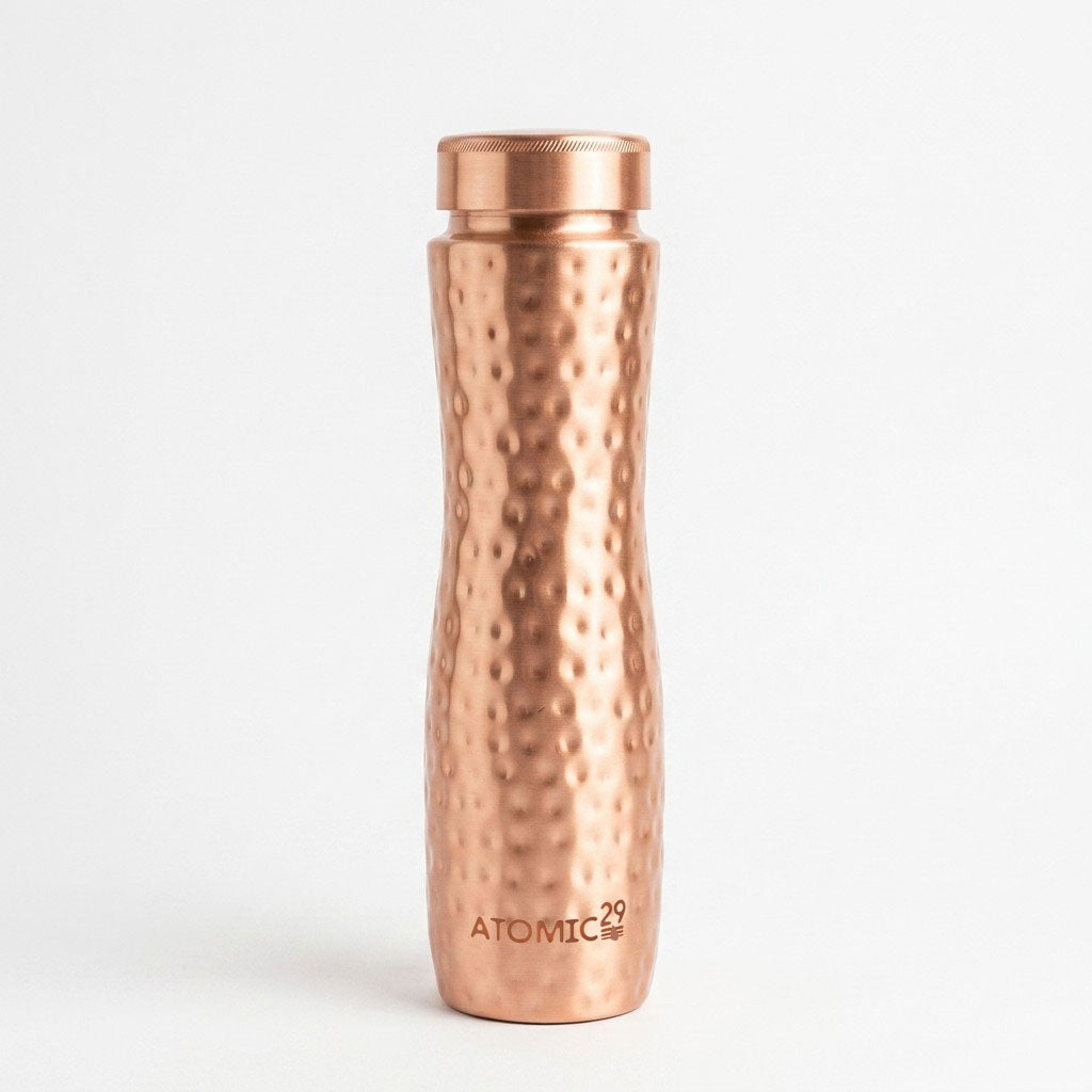 A hammered curve copper water bottle with a matching metallic cap, standing upright on a clean white background. The brand name 'ATOMIC29' is printed near the bottom.