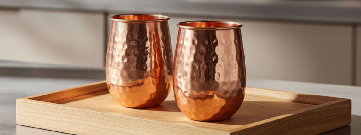 Two copper tumblers on a wooden tray with a neutral background