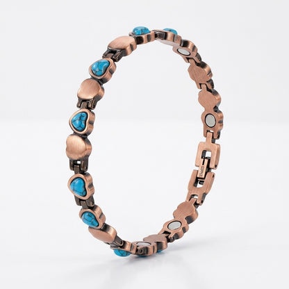 A heart-link copper magnetic therapy bracelet, accented with small heart shaped turquoise blue stones, shown on a light grey background.