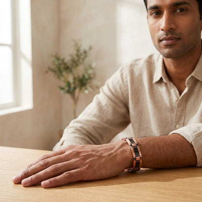 A man wearing a slim copper bracelet with carbon fibre inlays, resting his hand on a wooden table in a bright, modern room.