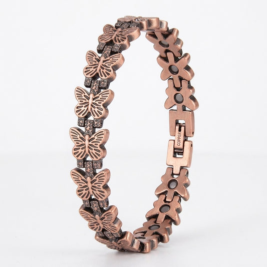 A copper magnetic bracelet featuring alternating butterfly links, accented with small clear crystals and black round details, shown on a light grey background.